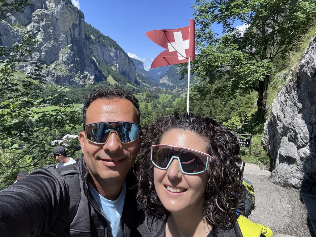 Pareja de viajeros ante un valle alpino con bandera de Suiza